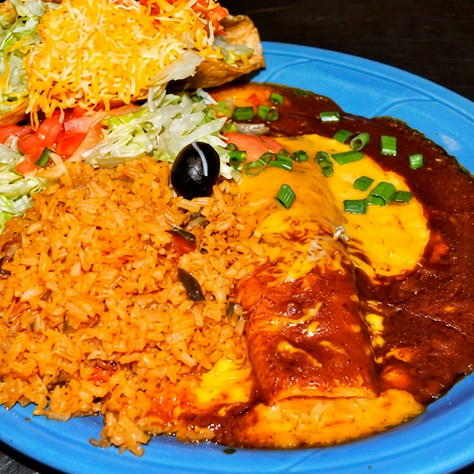 Mexican platter with enchiladas, seasoned rice, refried beans, taco, lettuce, tomatoes, shredded cheese, and black olives on a blue plate.